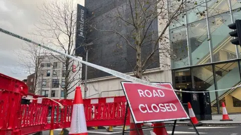 A road closed sign with bollards and cones outside Exeter's John Lewis building.