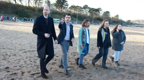 PA Media Prince William on the beach in a long black jacket with three young people