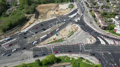 An aerial view of Dawsons Corner junction in Leeds where a new junction is being built. Fresh tarmac has been laid, but some parts of the road are still under construction.
