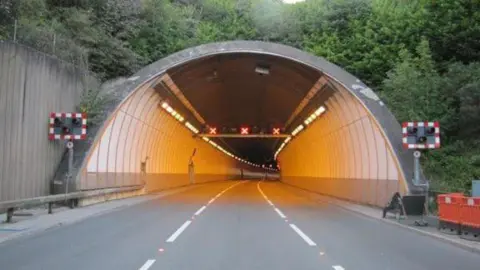 The tunnel with lights shining on either side of it and two white broken up lines travelling down the road