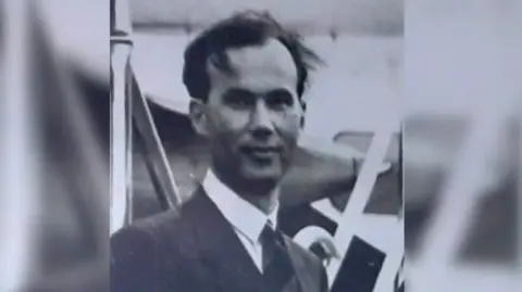 Other Black and white image of James Sayers. He is looking at the camera and wearing a suit.