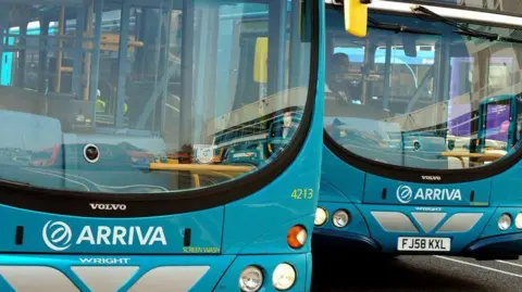 A turquoise bus parked at a bus stop, with passengers queuing to board.