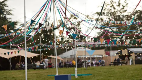 Getty Images Colourful bunting and fairy lights are strung up between flagpoles with festival huts and trees in the background.
