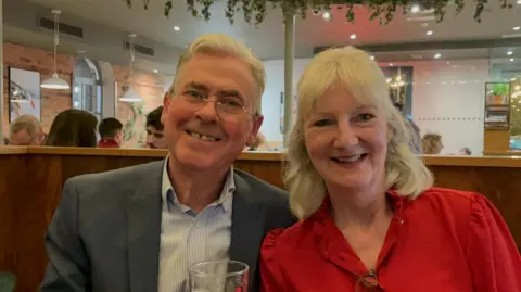 Supplied A photograph of a couple in a restaurant. The man on the left wears a shirt and a suit and the woman is wearing a red blouse. 