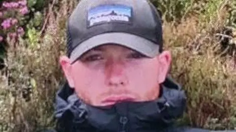 Police Scotland Shane Donnelly or Barr, a young man wearing a black cap and black jacket with visible red stubble on his face