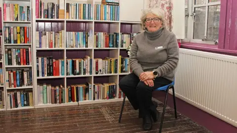 Wanlockhead Community Centre Carole Kilshaw from the Wanlockhead Community Centre sitting in a chair wearing a grey polo-neck knitted jumper and black trousers 
