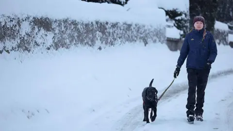 Getty Images A woman walks a dog along a snowy road towards the camera