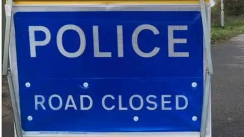 A police road closed sign with a blue background on a road.