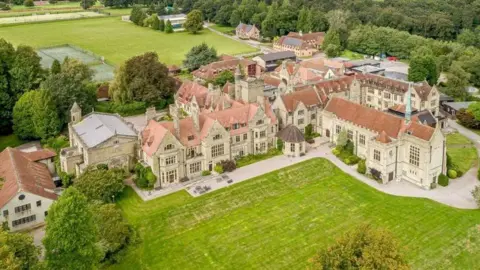 A drone shot of the outside of the school which consists of large green grounds and multiple large brick buildings