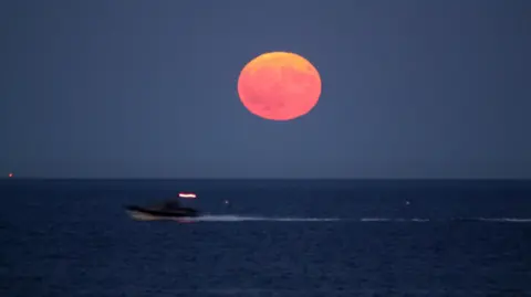 Brian A speedboat blurs across the foreground, with the moon above.