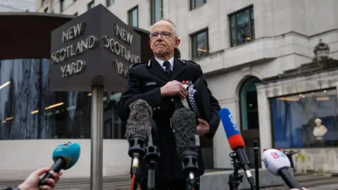 Getty Images Sir Mark Rowley stands in front of a bank of microphones outside New Scotland Yard. He is in police uniform.