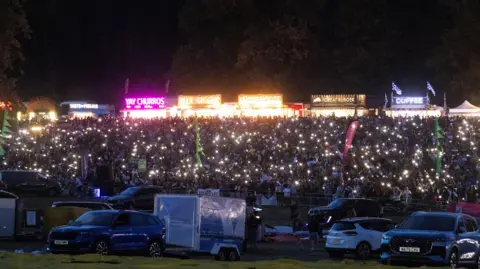Paul Box A large crowd at the Bristol Balloon Fiesta hold up their phones creating hundreds of points of light in the darkness