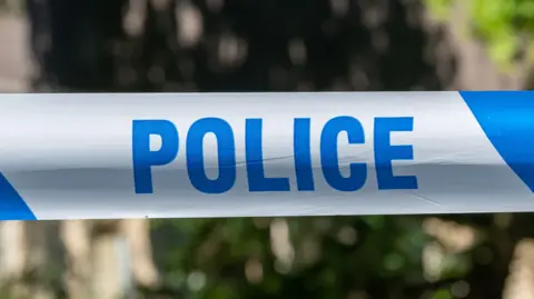 A close-up of a section of blue-and-white striped police tape. The word POLICE is in capital letters in blue. The background is out of focus.