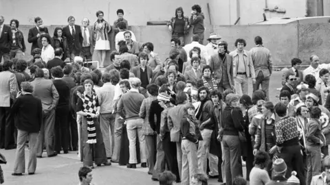 Getty Images Fans queue outside Wembley with many wearing scarves and flares.
