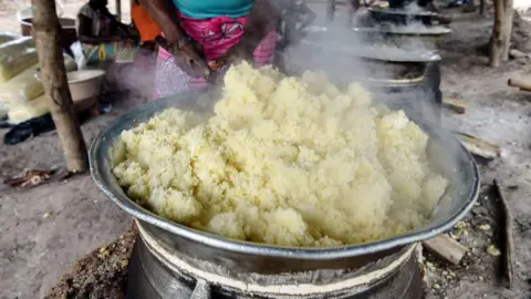 AFP A woman prepares attiéké in a large steel pot