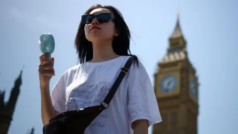 A woman uses a fan as she walks near the Houses of Parliament