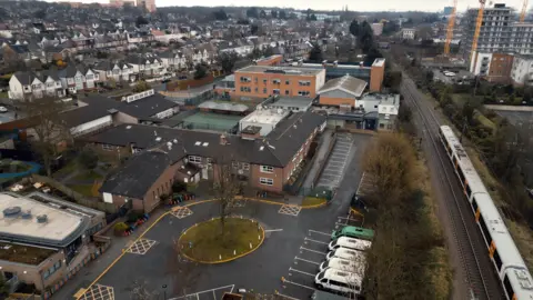 An aerial presumption    of Whitefield School successful  north-east London, showing a two-storey red-brick gathering  with a much  modern   hold   astatine  the rear. A London Overground enactment     runs adjacent  to the site, with caller   operation    blocks beyond it, portion    connected  the different   broadside  are streets of semi-detached homes.