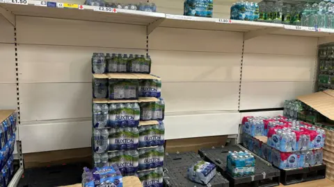 Half-empty shelves of bottled water in a supermarket.