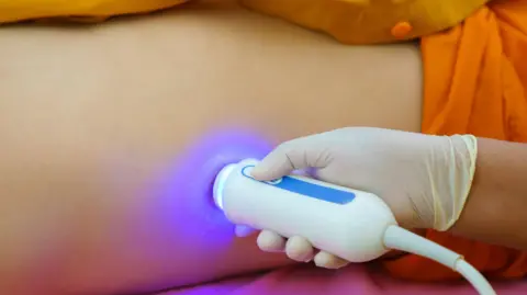 A person wearing a latex glove holding a scanner to the side of a person's body. The scanner is emitting a blue light.