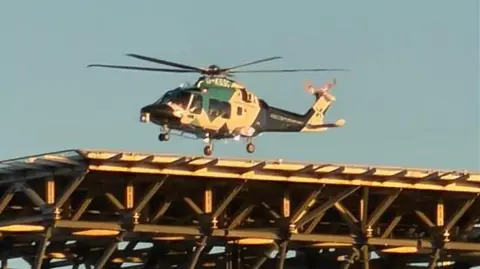 A blue and white Air Ambulance landing on a raised helipad.