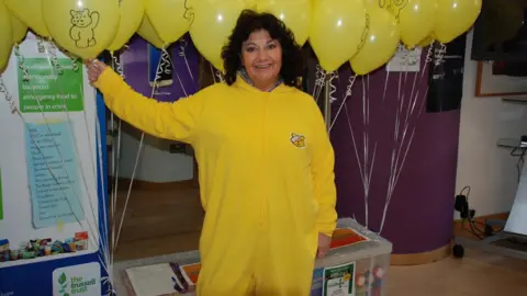 Alun Williams A smiling woman in a yellow onesie holding a set of balloons