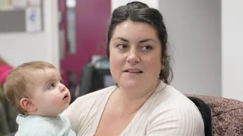 Joanne Wilkinson sits on a chair holding her daughter, Adeline.