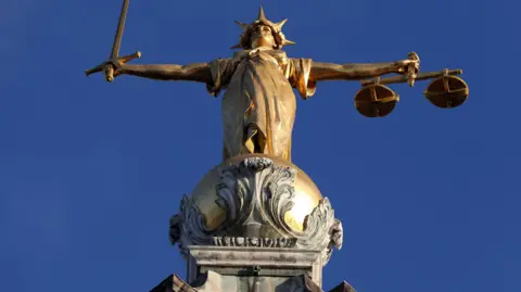 A statue representing justice, holding a sword in one hand and scales in the other, standing above the Old Bailey in London