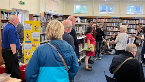 Shariqua Ahmed / BBC People standing and talking in the library surrounded by bookshelves full of books