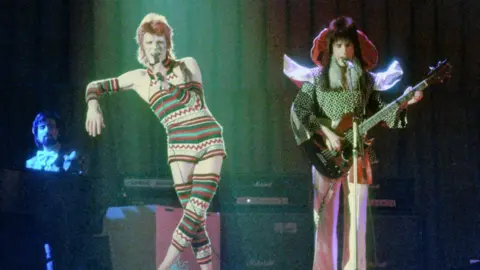 Getty Images David Bowie on stage in the 1970s dressed in a knitted one piece costume. 