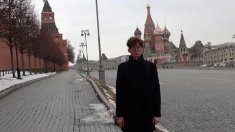 Lik family Kevin standing in Red Square in Moscow with the Kremlin wall on one side and St Basil's Cathedral behind him