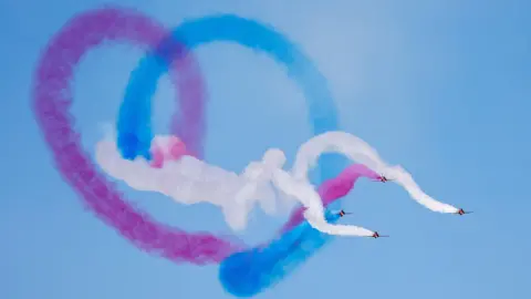 VisitBlackpool Four Red Arrows planes fly in formation, leaving a red, white and blue smoke heart behind them