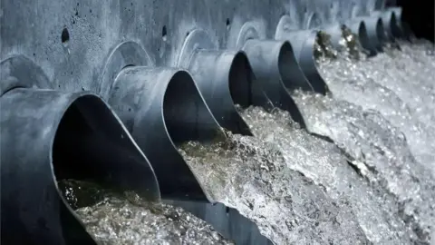 Getty Images Ten large black tubes with dirty water flowing from them