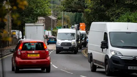 Several vehicles sit in slow moving or stationary traffic on the A57. It is a road with only one lane travelling in each direction.