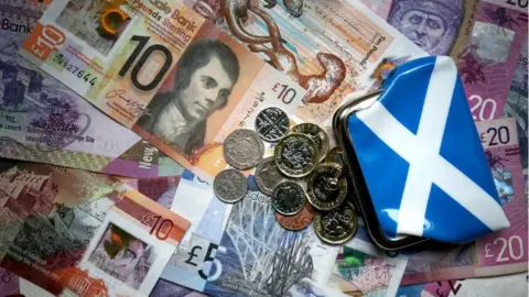 PA Media A pile of Scottish banknote and coins next to a saltire coin purse