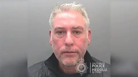 South Wales Police A police mugshot of a man with short grey hair and stubble. In the corner is a logo for South Wales Police.