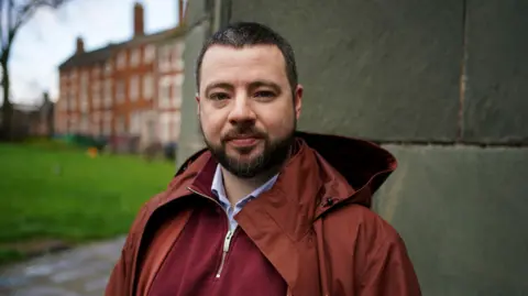 PA Media Jason Evans, wearing a maroon jumper and a terracotta coat.