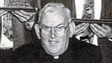 Pacemaker A black and white photo of the late Fr Malachy Finegan.  He had short white hair and glasses and was wearing a black suit and a priest's collar.