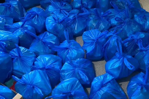 Imran Bahar Rows of blue carrier bags full of food are laid out on the floor.