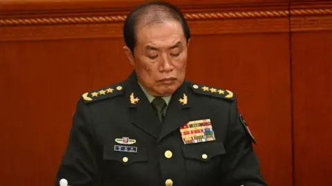 AFP via Getty Images He Weidong dressed in full military regalia looks down as he sits in the Great Hall of the People in Beijing