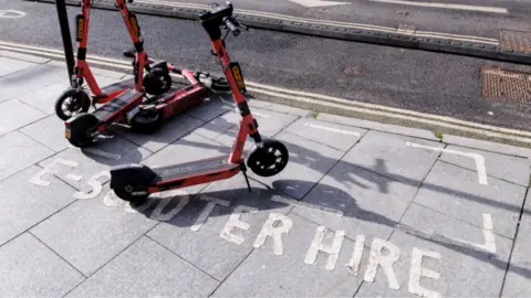 E-scooters on a pavement which has the words 'e-scooter hire' printed on 