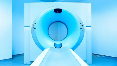 The front view of a CT scan machine, in an empty, blue room