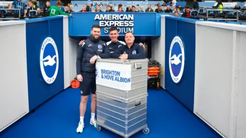 Three members of the Brighton and Hove Albion kit team stand in the tunnel at the Amex Stadium.