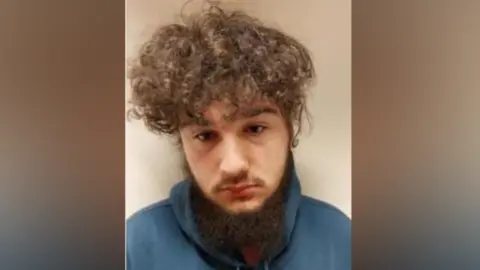 Lancashire Police Leon Callaghan, with frizzy brown hair and a beard, looks straight ahead in his police mugshot