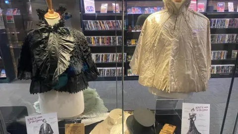 Costumes in a display cabinet. They are one black one white opera cape.