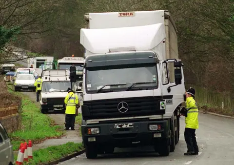 Alamy West Mercia Police officers wearing yellow high-vis jackets stand at the side of a white Mercedes lorry by the side of a road
