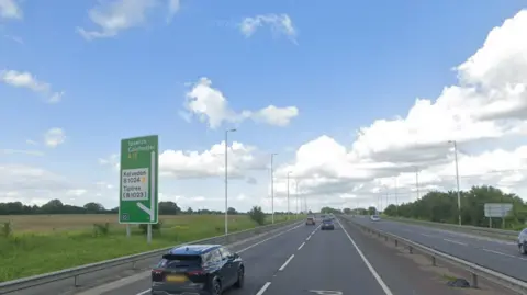 Google Google Maps image of the A12 near Kelvedon showing a large green sign to highlight the Kelvedon exit. The roads in this image are relatively clear and the sky is blue with some clouds.