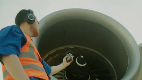 Musician Jordan Rakei in a safety vest and headphones records the sound of a jet engine.
