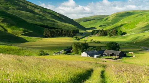 Northumberland National Park  An image of a green valley with a farm in the foreground 