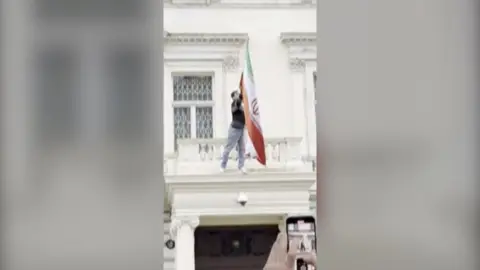 A protester is on the balcony of the Iranian embassy, tearing down a flag