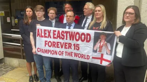 Anna Jameson/BBC Members of the Eastwood family hold a banner tribute to Alex Eastwood